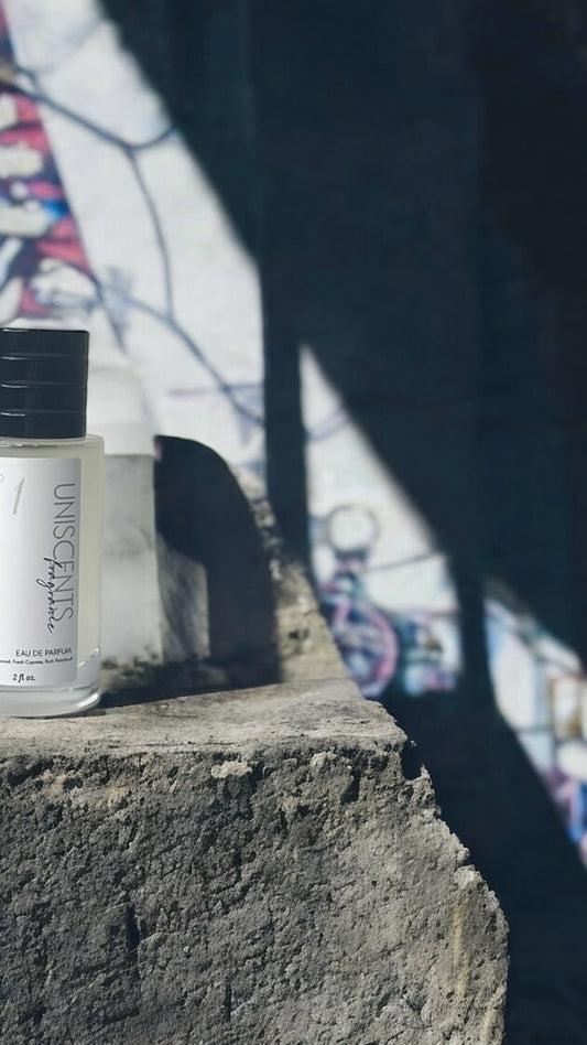 A small, clear glass bottle with a black cap, labeled ' uniscents No. 1', containing a yellowish liquid, placed against a light background.