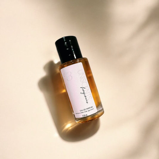 A perfume bottle with a clear liquid visible inside, labeled 'uniscents No. 3', placed on a white surface with a shadow cast over it.